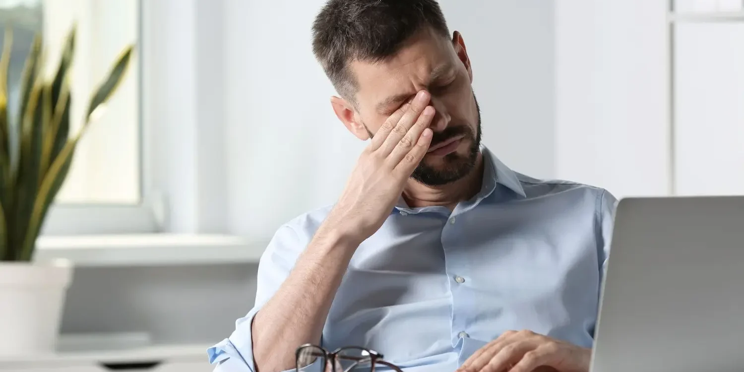 Man suffering from eyestrain at desk in office